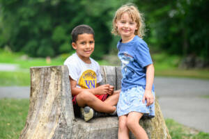 A pair of summer camp attendees rest on a tree stump.